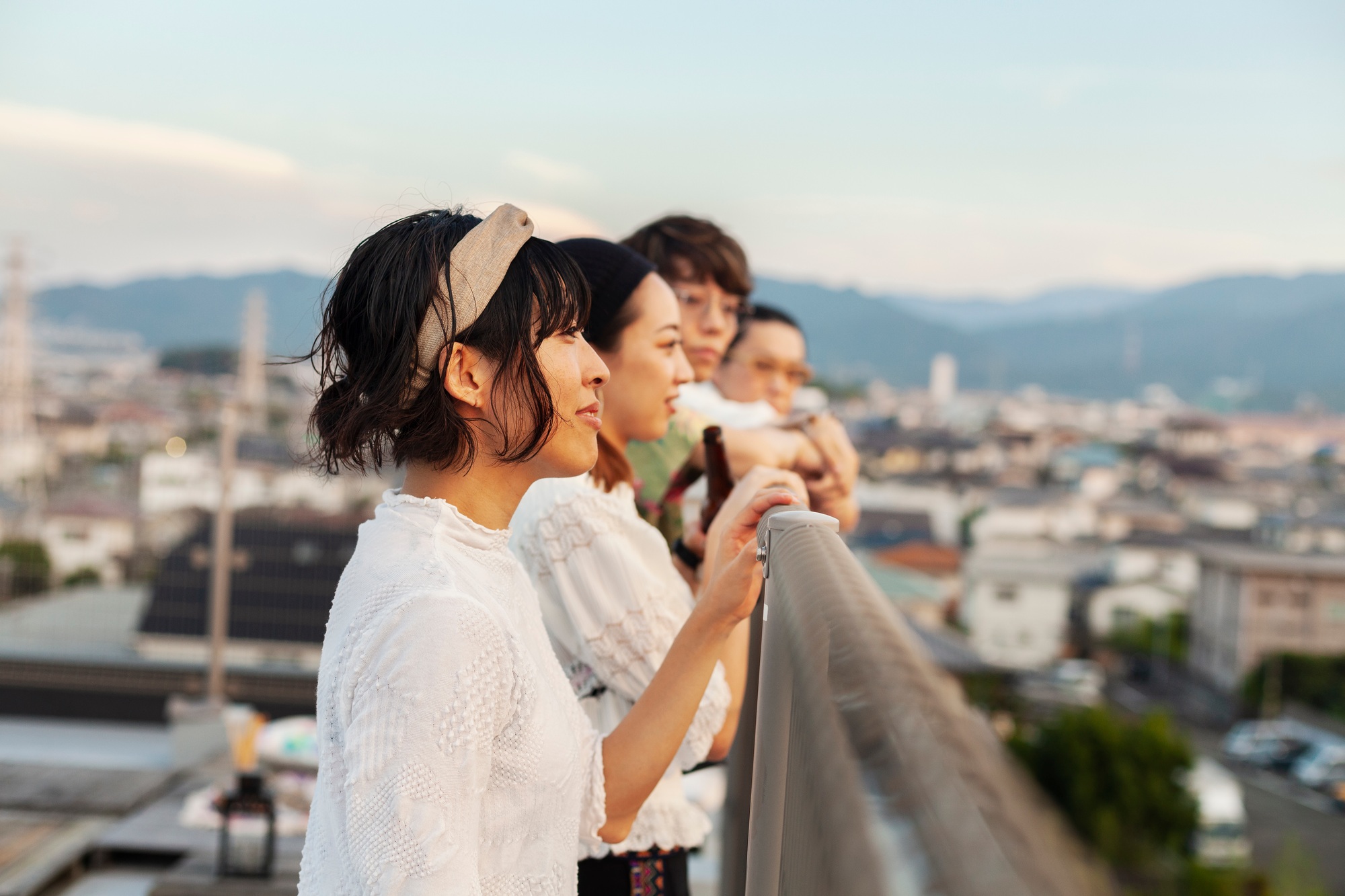 Group of young Japanese men and women standing on a rooftop in an urban setting.